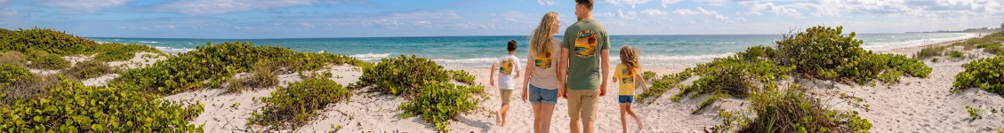 Family walking along a sandy beach with the ocean in the background.